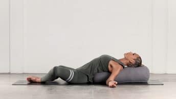 Abi Carver practicing a supported yin yoga pose, lying on a bolster with knees open to the sides